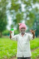 indiano feliz agricultor segurando esvaziar garrafa dentro mãos, feliz agricultor mostrando branco garrafa foto