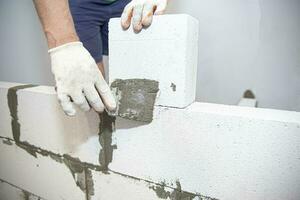 reboco a parede.mão segurando uma espátula com construção misturar.aplicando massa de vidraceiro ou telha cola para com leve concreto blocos.gesso a parede com uma massa de vidraceiro faca interna construção foto