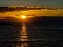 sol se pondo na praia de muriwai, auckland, nova zelândia foto