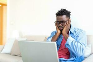 frustrado jovem africano empreendedor com triste careta dentro frente do dele computador portátil dentro escritório, notado uma grande erro ele fez, segurando dele cabeça com braços Palmeiras foto