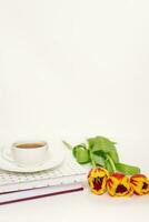 Primavera cumprimento cartão. cadernos, uma ramalhete do tulipas e uma copo do chá em uma branco fundo com cópia de espaço foto