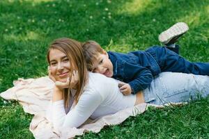 pequeno Garoto e dele mãe estão relaxante dentro a parque dentro a verão deitado em a Relva e tendo Diversão foto