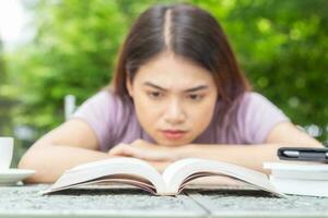 fechar-se frente Visão do ásia mulher lendo uma livro dentro a quintal mostrar muitos emoções foto