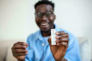 afro-americano homem segurando uma negativo teste dispositivo. feliz jovem homem mostrando dele negativo coronavírus - covid-19 rápido teste. coronavírus foto