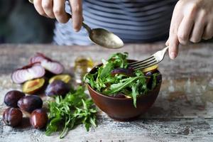 salada saudável misture as mãos masculinas com uma colher e um garfo. salada de ameixa de rúcula.