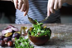 salada saudável misture as mãos masculinas com uma colher e um garfo. salada de ameixa de rúcula.