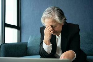 sobrecarregado cansado velho senhora segurando cabeça sentindo-me dor de cabeça. ásia Senior o negócio mulher estresse a partir de Difícil trabalhar. frustrado o negócio mulher pensa sentado às ambiente de trabalho, sentir angustiado parece desamparado conceito foto