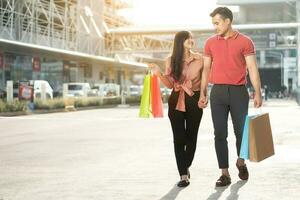 casal jovem feliz de compradores andando na rua comercial em direção e segurando sacolas coloridas na mão. conceito de venda e compras de sexta-feira negra foto