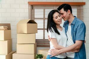 sorridente jovem ásia feliz casal abraçando namorado com cartão caixas às comovente dia dentro seus Novo casa depois de comprando real Estado. conceito do iniciando uma Novo vida para uma recentemente casado casal. foto