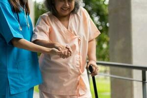 ásia Cuidado cuidador ou enfermeira aguarde paciente mão e encorajar paciente, caminhando dentro jardim. conceito do feliz aposentadoria com Cuidado a partir de uma cuidador e poupança e Senior saúde seguro. foto