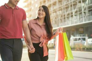 casal jovem feliz de compradores andando na rua comercial em direção e segurando sacolas coloridas na mão. conceito de venda e compras de sexta-feira negra foto