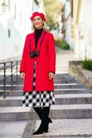 à moda mulher dentro vermelho casaco em pé em cidade rua dentro luz solar foto