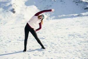 fino mulher dentro roupa de esporte alongamento braço lateralmente dentro Nevado montanhas foto