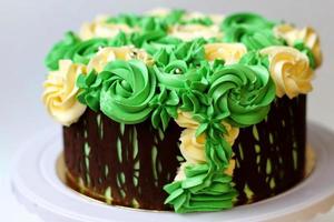 lindo bolo caseiro coberto de rosas amarelas e verdes feito de creme de manteiga, moldura de chocolate, glacê no fundo branco foto