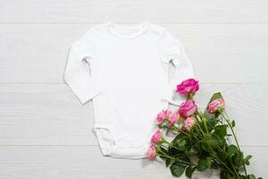 branco brincar recém-nascido camisa. de madeira fundo, Rosa rosas, feliz aniversário. em branco modelo macacão maiô frente topo visualizar. bebê roupas. ramalhete do flores foto