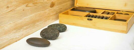 Preto massagem pedras deitado perto a de madeira caixa com massagem pedras em a toalha em a mesa. foto