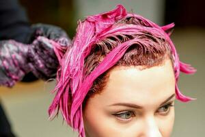 a profissional cabeleireiro usa uma escova para Aplique a Rosa corante para a cabelo. cabelo coloração conceito. foto