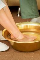 fêmea pés dentro uma dourado tigela com água dentro spa salão. spa tratamento. foto