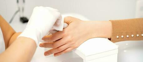 mãos do uma manicuro dentro branco protetora luvas limpar fêmea unhas com uma papel guardanapo dentro a salão. foto