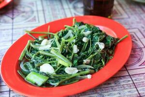 cah kangkung tumis, mexer fritar água espinafre em vermelho placa. foto