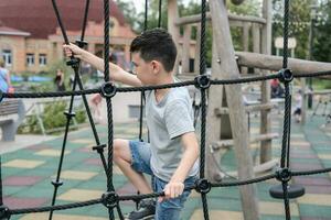 uma Garoto sobe acima a alpino rede em uma Parque infantil foto