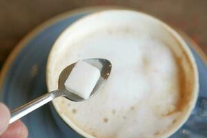 derramando branco açúcar cubo dentro uma café copo foto