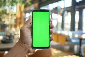 mão de jovem usando telefone inteligente com tela verde no café foto