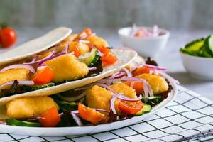 tortilla com frango pepitas, vegetais, cebolas e alface em uma prato foto