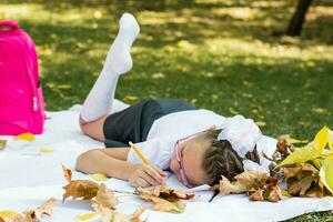 cansado do trabalho de casa, uma estudante caiu adormecido em uma cobertor dentro a outono ensolarado parque. ao ar livre Educação. costas para escola conceito foto