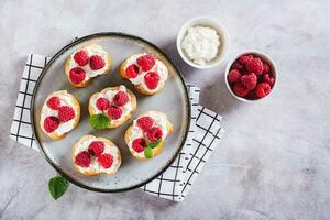 apetitoso crostini com ricota, framboesas e hortelã em uma prato em a mesa topo Visão foto