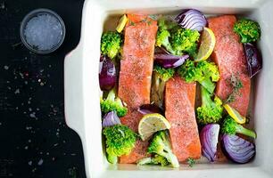 salmão, brócolis e vermelho cebola fatias estão preparado dentro uma cozimento prato. topo visualizar, a sobrecarga foto