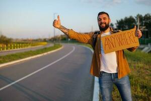 homem é pedindo carona em beira da estrada tentando para Pare carro. ele é segurando cartão com inscrição. foto