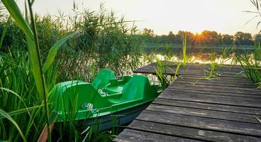 pedal bicicleta amarrado baixa para de madeira cais. nascer do sol sobre a lago. panorama às a lago com juncos. laranja céu. foto