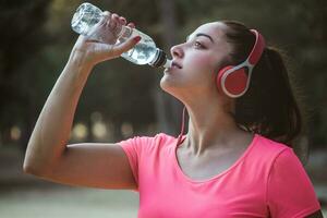 mulher bebendo água depois de exercício e ouvindo para música com alguns capacetes dentro a parque foto