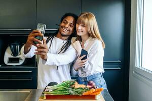 africano americano Garoto e branco menina fazer uma selfie dentro a cozinha foto
