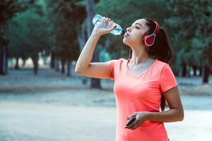 mulher bebendo água a partir de uma garrafa e ouvindo para música enquanto exercício foto