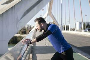 uma fechar-se tiro do uma jovem masculino inclinado em a fronteira do a ponte enquanto corrida foto