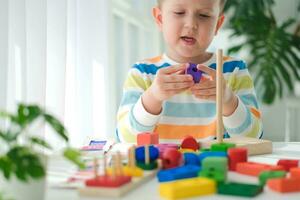 uma pequeno Garoto tocam com de madeira brinquedos e constrói uma torre. educacional lógica brinquedos para crianças. montessori jogos para criança desenvolvimento. crianças de madeira brinquedo. foto