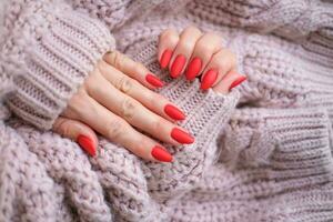 mulheres mãos com uma lindo fosco oval manicure dentro uma caloroso Rosa tricotado suéter. inverno tendência, cobrir vermelho unhas com gel polonês, shellac. direito autoral. foto