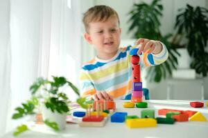 uma pequeno Garoto tocam com de madeira brinquedos e constrói uma torre. educacional lógica brinquedos para crianças. montessori jogos para criança desenvolvimento. crianças de madeira brinquedo. foto