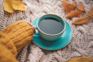 a garotas mão detém uma copo do café em uma tricotado fundo. chá e laranja folhas em a outono fundo. foto