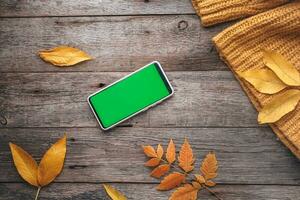 Móvel telefone com uma verde tela em uma de madeira outono fundo. Smartphone outono amarelo folhas. cópia de espaço. foto