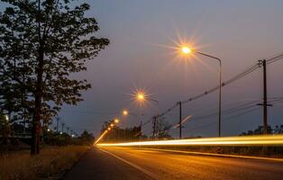 uma Visão do laranja explosão estelar a partir de uma poste de iluminação ao lado uma estrada com a luz do uma passagem carro. foto