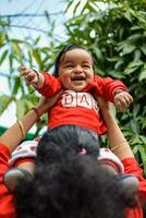 amoroso mãe carregando do dela bebê às sociedade parque. brilhante retrato do feliz mãe segurando criança dentro dela mãos. mãe abraçando dela pequeno 9 meses velho filho. foto