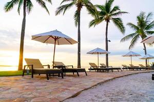 guarda-chuva e cadeira ao redor da piscina em hotel resort com nascer do sol pela manhã foto