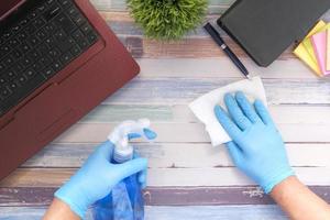 mão com luvas de borracha azul segurando frasco spray para limpar a mesa foto