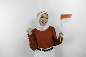 uma jovem ásia muçulmano mulher com uma feliz bem sucedido expressão vestindo vermelho topo e branco hijab enquanto segurando da indonésia bandeira, isolado de branco fundo. da indonésia independência dia conceito. foto