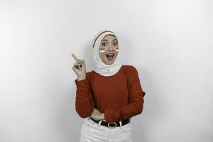uma feliz ásia muçulmano mulher vestindo branco hijab e vermelho principal, e apontando cópia de espaço em topo do dela, isolado de branco fundo. da indonésia independência dia foto