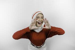 jovem lindo muçulmano mulher vestindo uma vermelho topo e branco hijab é gritando e gritando alto com uma mão em dela boca. da indonésia independência dia conceito. foto