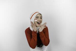 jovem lindo muçulmano mulher vestindo uma vermelho topo e branco hijab é gritando e gritando alto com uma mão em dela boca. da indonésia independência dia conceito. foto